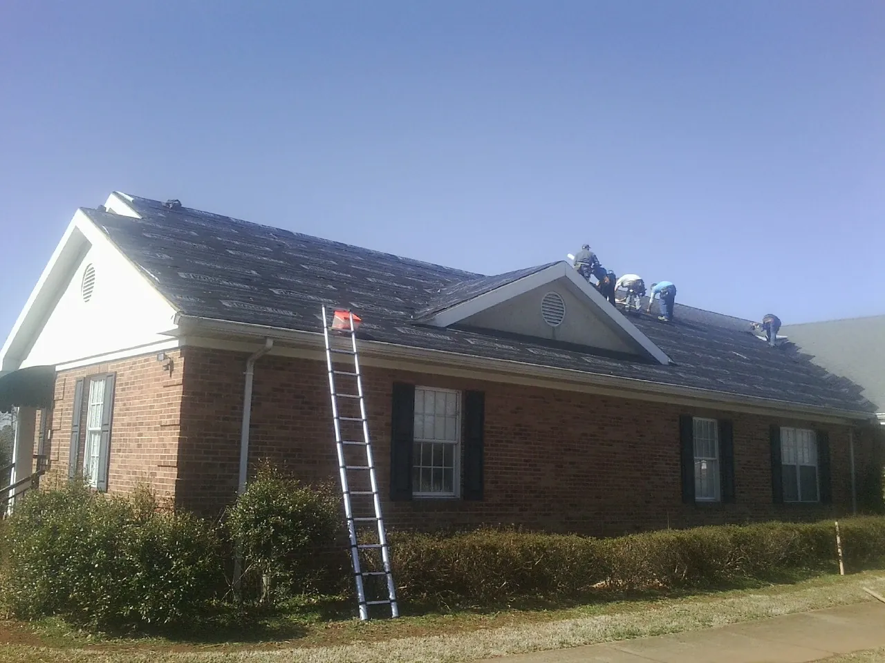 Crew tearing shingles off a brick ranch roof with a ladder set — Metal Roof Repair work by our crew in Fombell