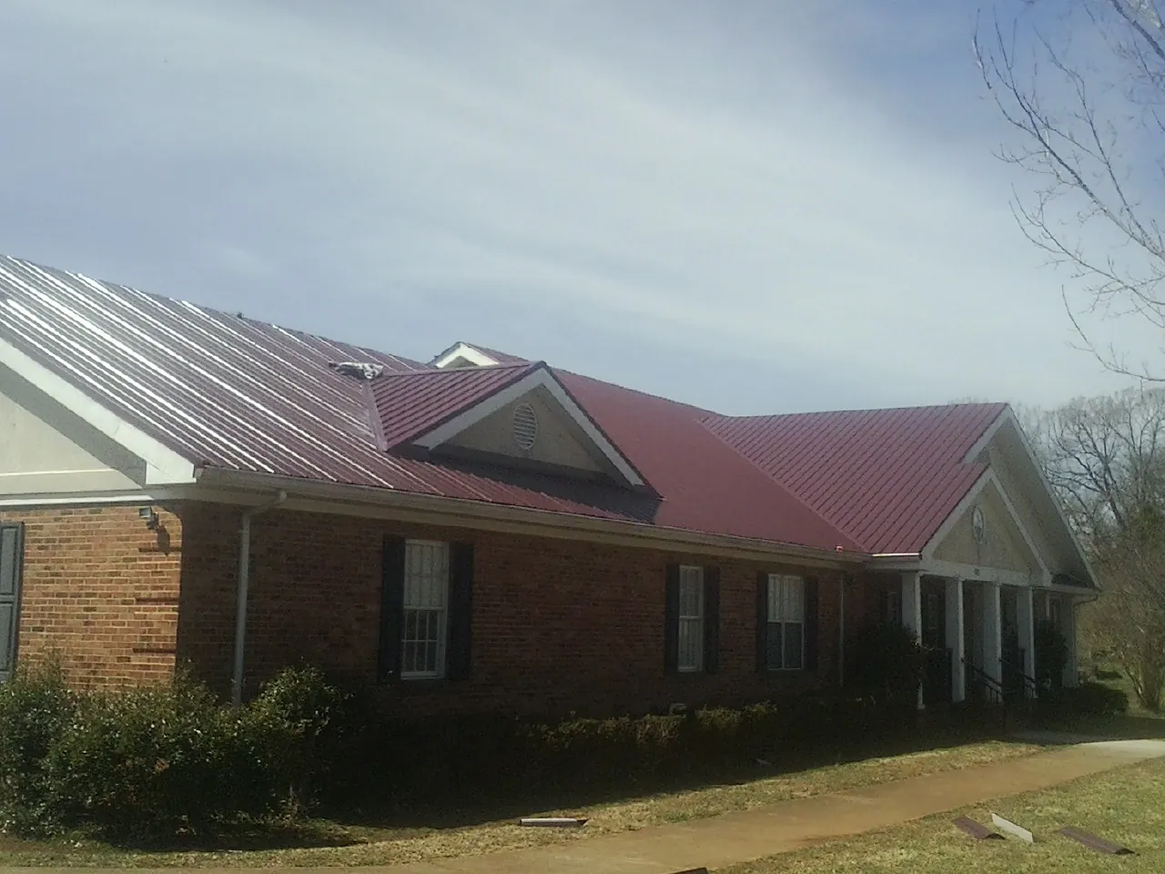 Red metal roof with gabled entries on a long brick building, from a Hail Damage Roof Repair job in Fombell