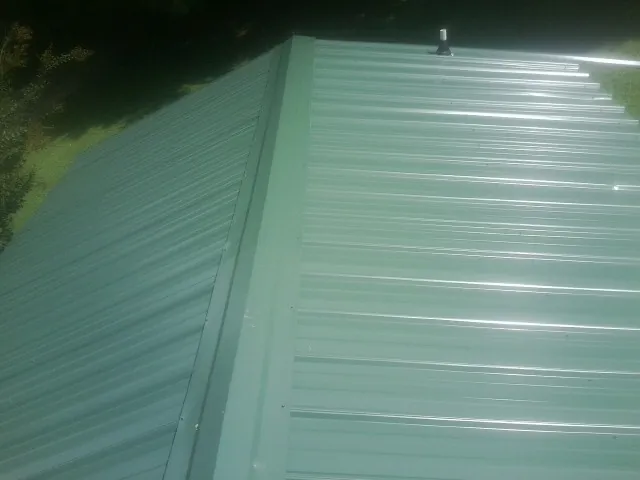 New green metal panels meeting at the ridge of a roof — Flat Roof Repair work by our crew in Fombell