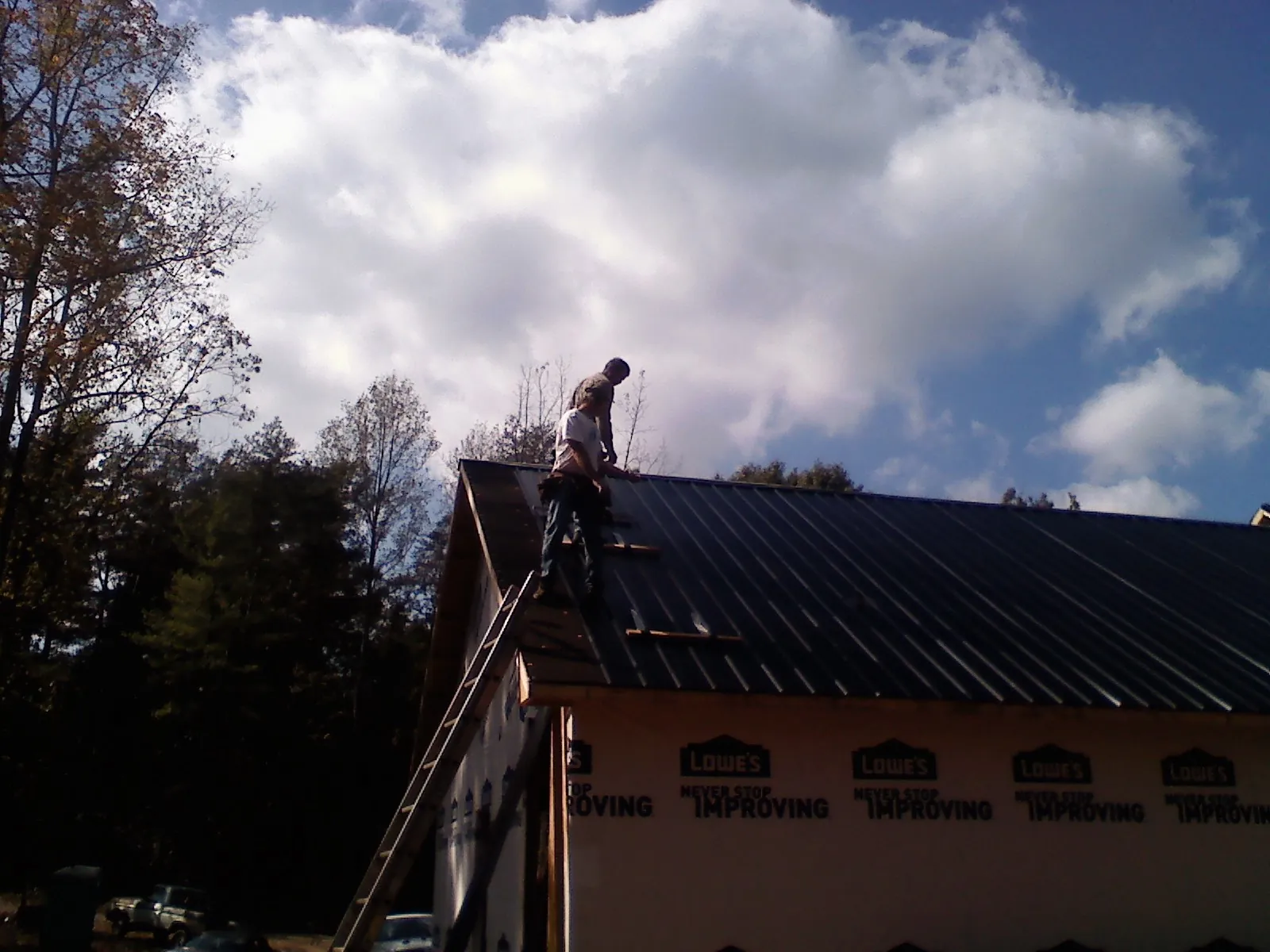 Roofer fastening dark metal panels high against a cloudy sky, from a Roof Inspection job in Fombell